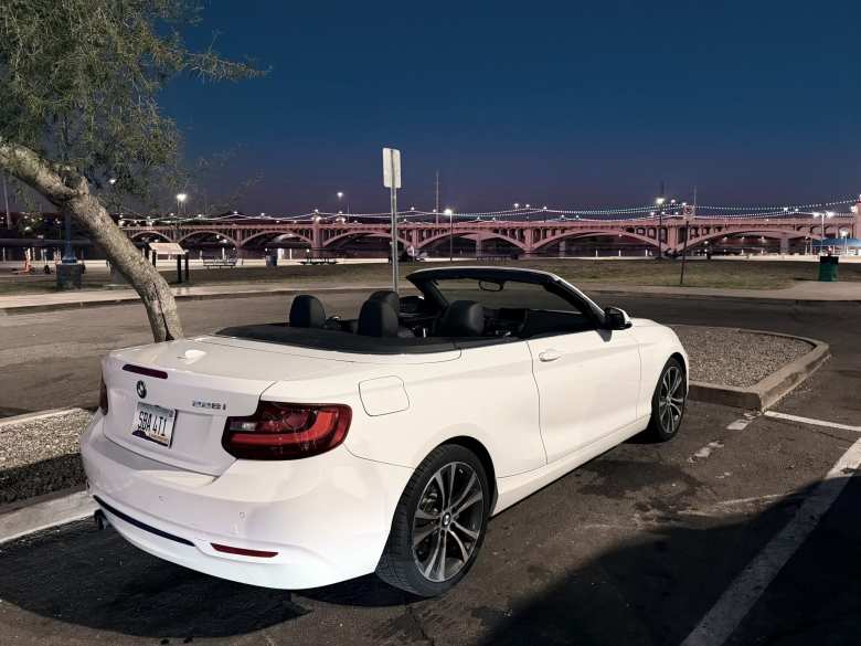 Rear three-quarters view of the Alpine White 2016 BMW 228i Turo rental with its top down.