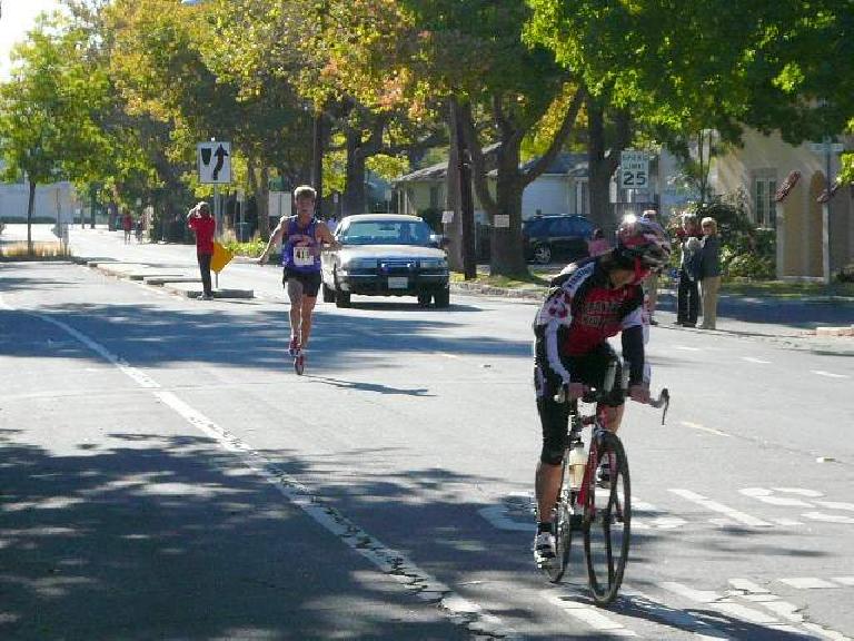 The first runner was so far ahead that he cruised into the finish behind this cyclist.