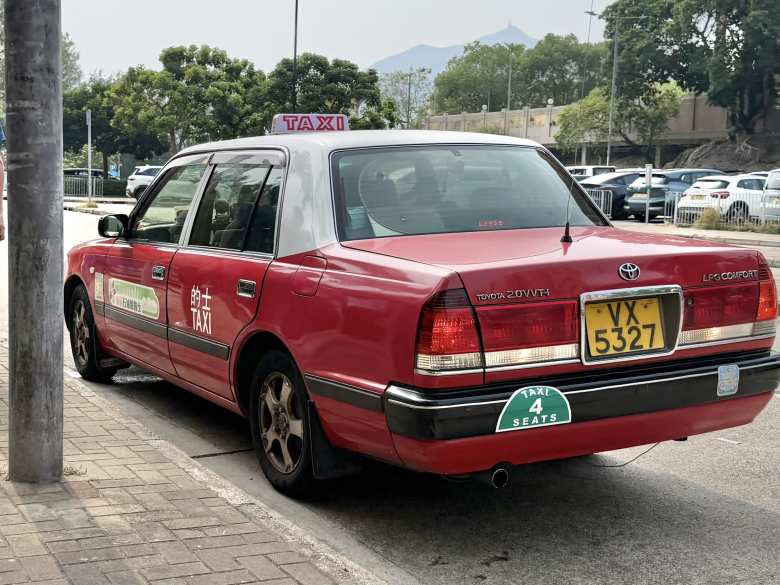 A red Toyota Comfort. These taxis have been the backbone of Hong Kong since 1995. The "2.0 VVT-i" badge on the trunk indicates this one is a later-production model (post-2008) which upgraded to the 1TR-FPE LPG engine.