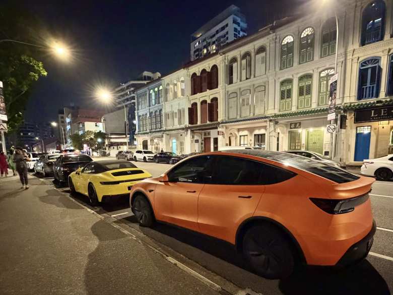 A yellow Porsche 911 and orange vinyl- wrapped Tesla Model Y in the Robertson Quay district of Singapore.