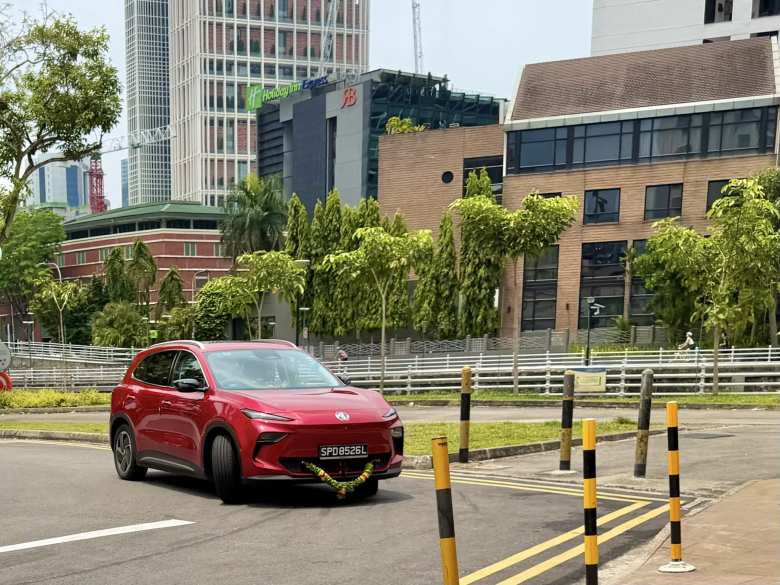 A red 2026 MGS5 EV wearing a traditional flower garland, a common sight in Singapore for a newly delivered vehicle's blessing. It has nearly 50/50 weight distribution, unusual for an SUV.