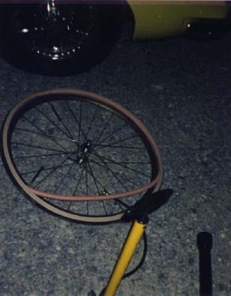 bicycle wheel on the ground with tire and tube off and a yellow bicycle pump at night