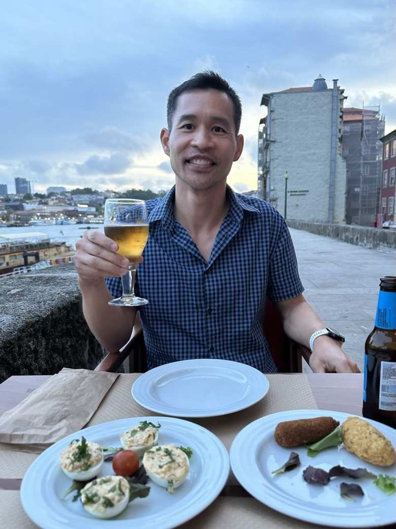 Felix with a glass of non-alcoholic beer, deviled eggs, and croquettes in Porto by the Rio Douro.