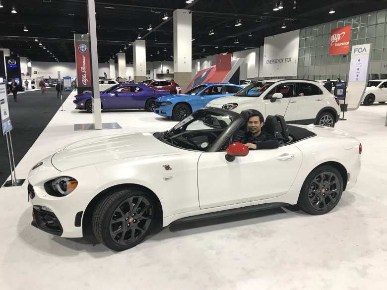 Felix sitting inside a white Abarth Spider at the 2019 Denver Auto Show.