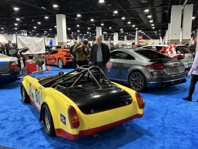 A yellow Austin-Healey Sprite with a grey Audi TT Coupe in the background.