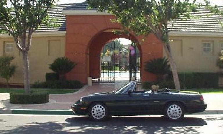 green 1991 Alfa Romeo Spider with top down in front of orange archway of HOA pool