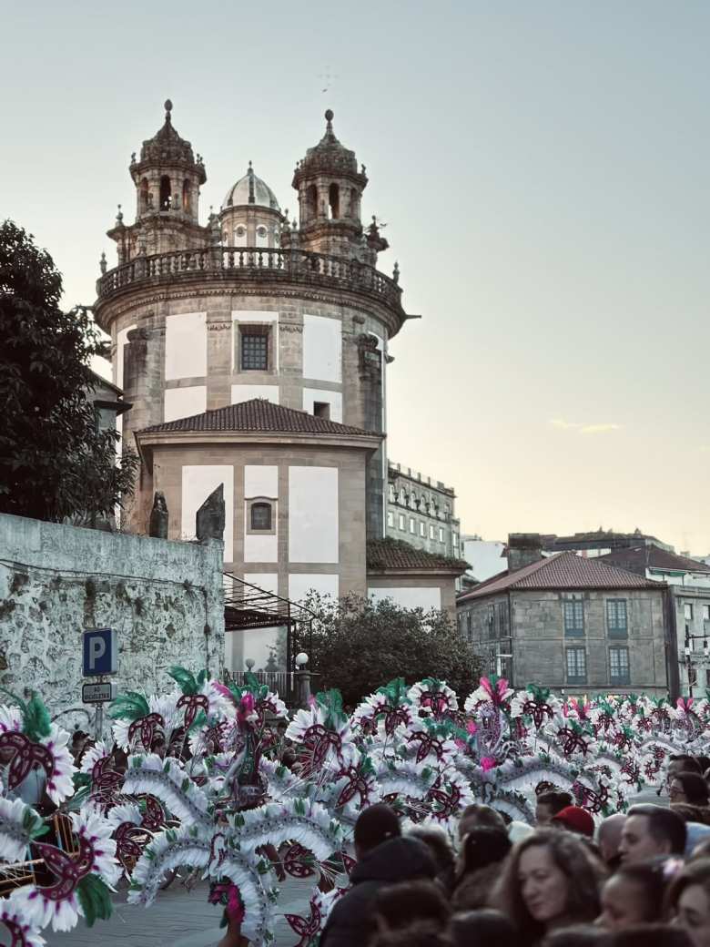 A parade of people dressed up in white feathered costumes passing by the Iglesia de la Virgen Peregrina in Pontevedra during Entroido.