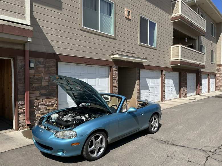 Manuel's sky blue NB Miata with the hood up at his apartment complex.