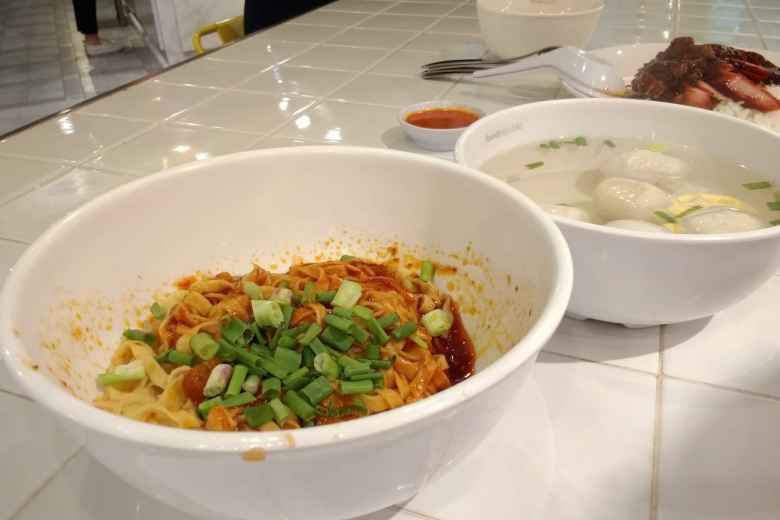 A noodle dish with a spicy sauce and green onions, meatballs in broth and barbecue pork over rice.