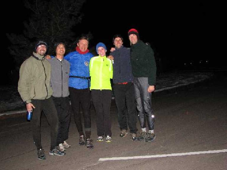 Five male and one female runner wearing winter clothes at a parking lot.