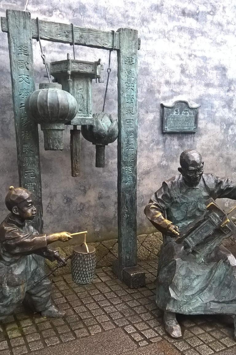 Statues of two Chinese people, one carrying a lantern and another some sort of musical instrument in Fuzhou, China.