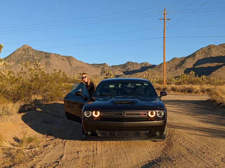 Andrea behind the open right door of a grey Dodge Challenger R/T in the Arizona desert.