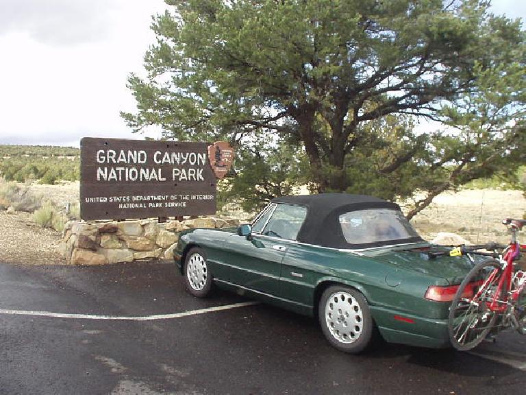 Green 1993 Alfa Romeo Spider Veloce with a red Cannondale R500 road bicycle in front of a Grand Canyon National Park sign.