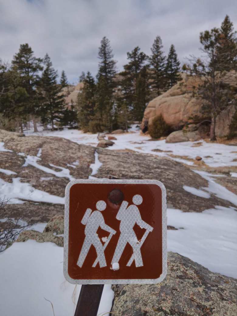 sign depicting two hikers, snow on rocky ground, evergreen trees