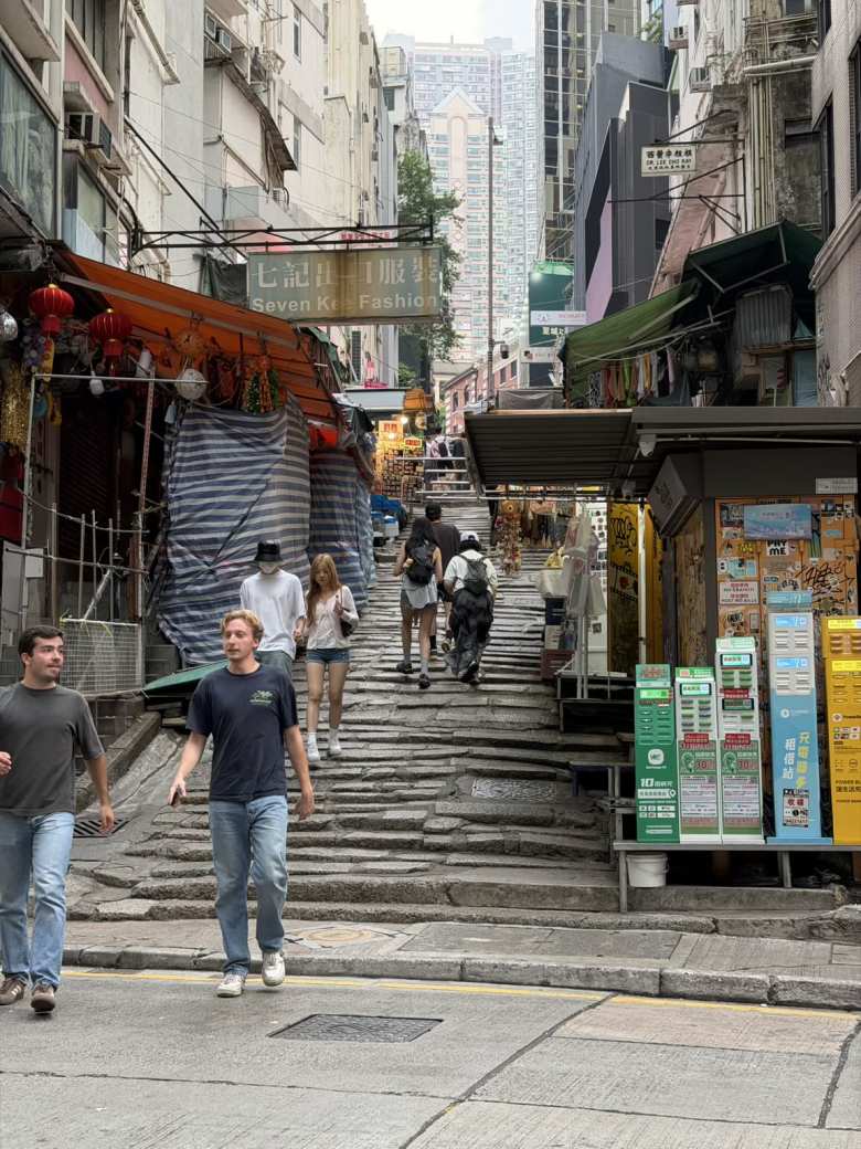 Pedestrians navigate the iconic, narrow stone steps of Pottinger Street amidst the vibrant market stalls of Central Hong Kong.