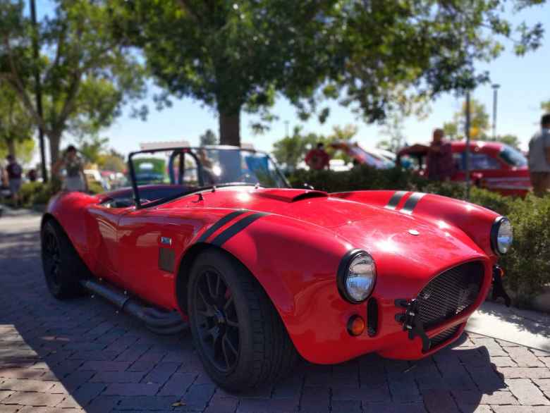 A red Shelby Cobra kit car with blacked-out chrome bits and matt black stripes.