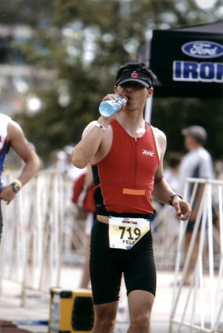 Felix Wong wearing red triathlon suit and black Ironman cap, drinking a bottle of blue Gatorade