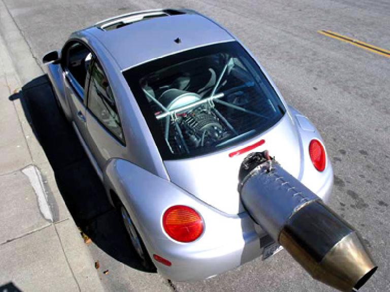 large jet engine sticking out of back of silver VN New Beetle.