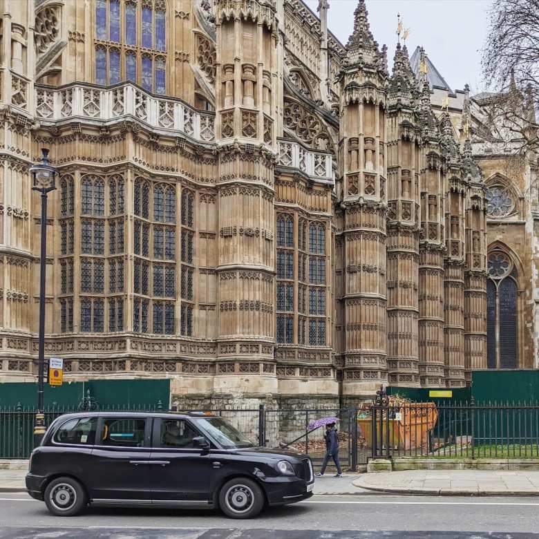 A black London Taxi driving by Westminster Abbey.