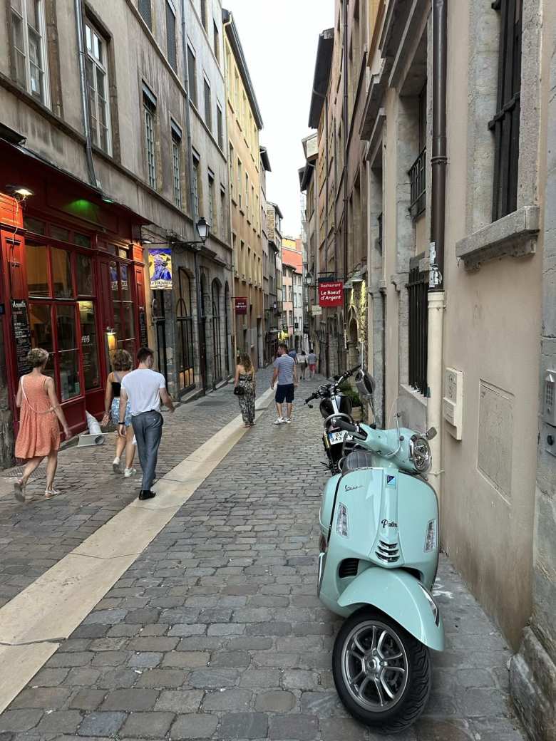 People walking by a turquoise Vespa motorbike on Rue du Boeuf in Old Lyon.