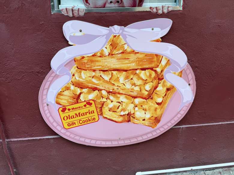 A cheerful, oversized sign for OlaMaria cookies highlights the sweet, almond-studded treats that are a local favorite in Macau.