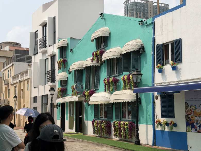 Cascades of purple and yellow flowers add a pop of natural beauty to the bright turquoise facade of this charming European-style building.