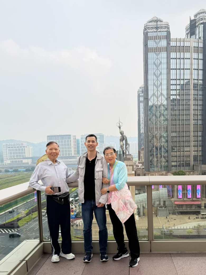 My dad, my aunt, and I stand on a balcony overlooking the Cotai Strip, with the Golden Muse statue and the towering heights of Studio City framing the skyline behind us.