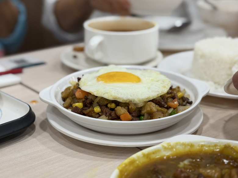 A steaming plate of Minchi, a beloved Macanese comfort food, features a savory mix of minced beef and diced potatoes tossed with peas, carrots, and corn, all finished with a signature fried egg on top.