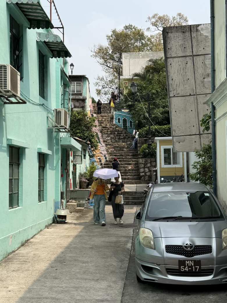 Two women protect themselves from the sun after walking down a stone stairway in Macau.