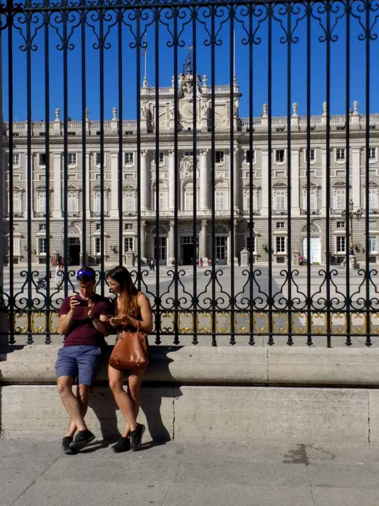 A man and woman looking at a smartphone in front of the Royal Palace of Madrid.