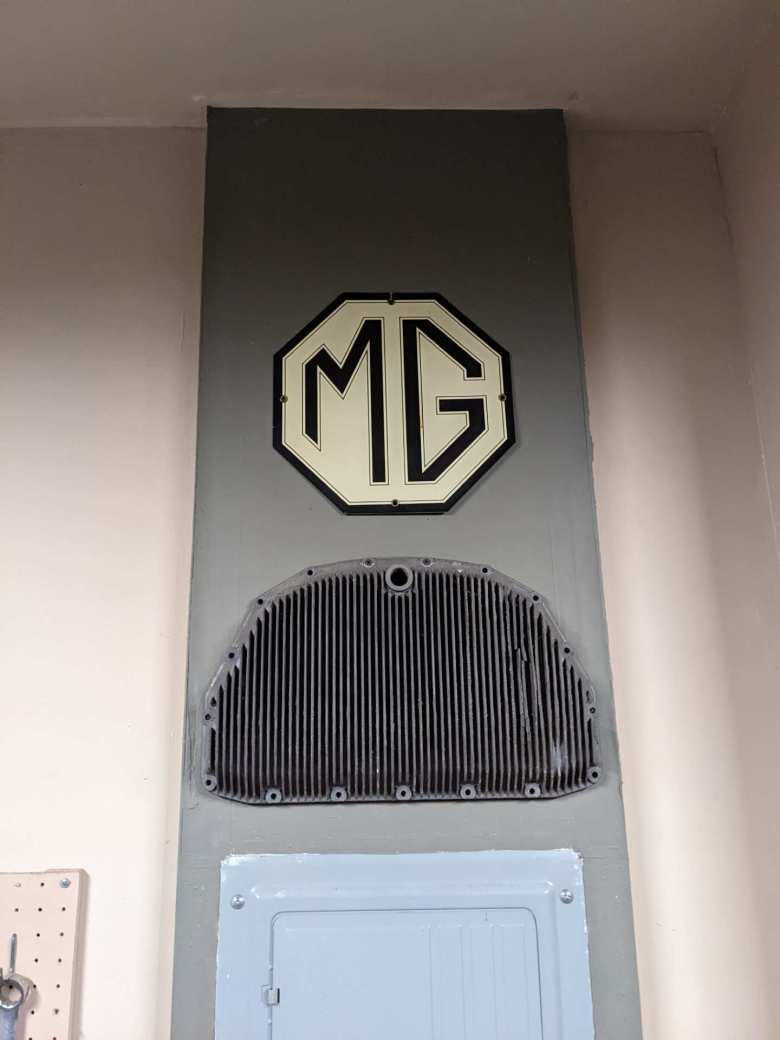 An MG sign above a cracked oil pan from my former 1991 Alfa Romeo Spider Veloce in the garage.