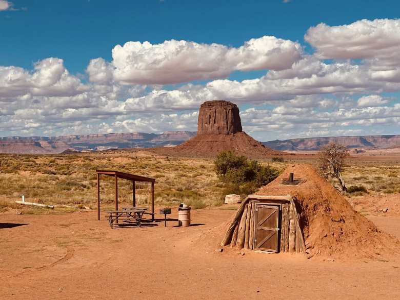 A shaded picnic area and a traditional Navajo hogan, with Mitchell Butte in the distance.