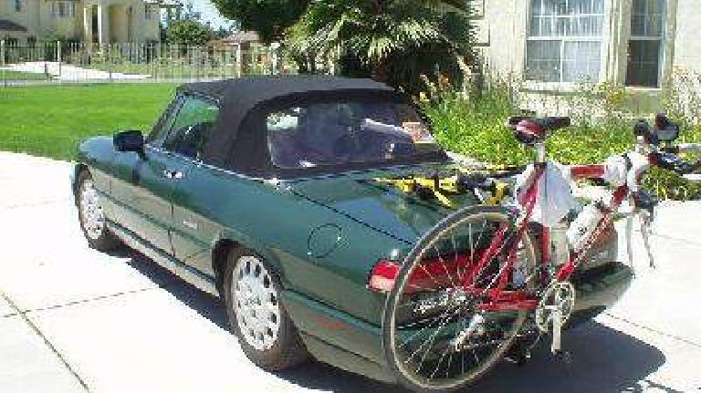 green 1991 Alfa Romeo Spider carrying red bicycle on bike rack