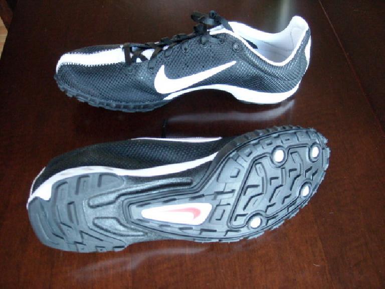 a pair of black and white Nike Zoom Waffle Racer VII shoes on a wooden table, with the sole of one visible