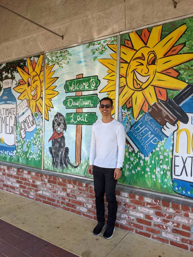 Felix Wong in front of a mural that says "Welcome to Downtown Lodi."