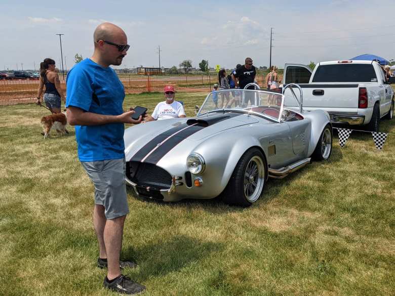 Manuel with a silver AC Cobra kit car with black racing stripes.