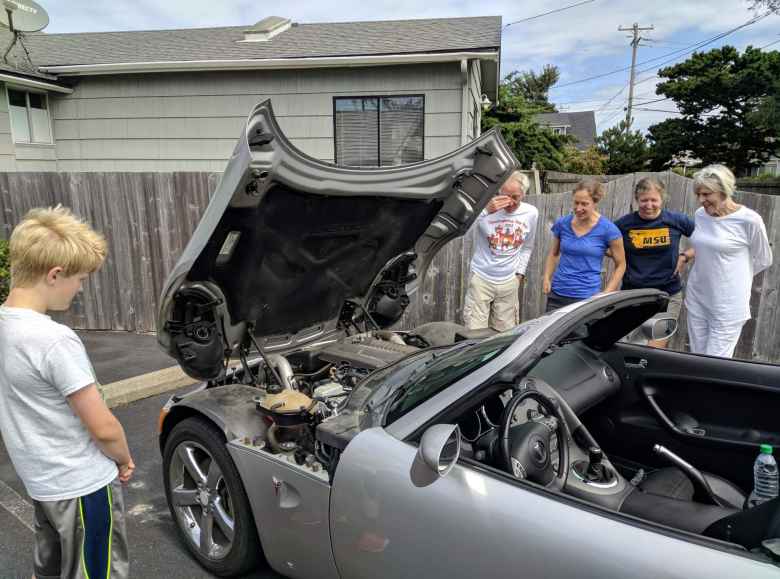 people looking at engine of silver Pontiac Solstice GXP with hood open