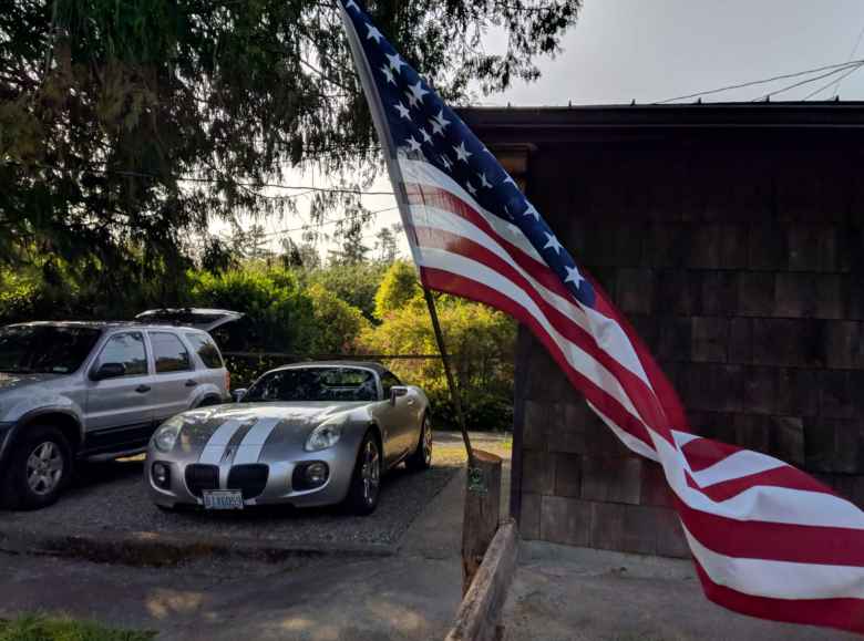 An American flag flying outside the house Erin and Russ are renting, with their silver Mercury Mariner and my silver Pontiac Solstice GXP rental car.