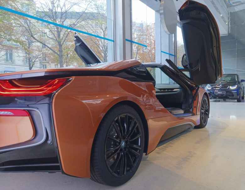 An orange BMW i8 inside the BMW showroom at George V. A dark blue BMW i3 is in the background.