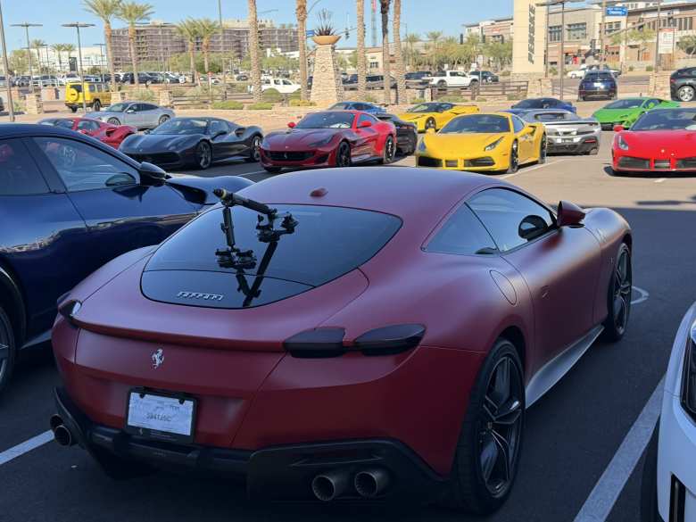 A matte red 2024 Ferrari Roma along with many other Ferraris (and a Porsche Taycan and Chevrolet Corvette) in the background.