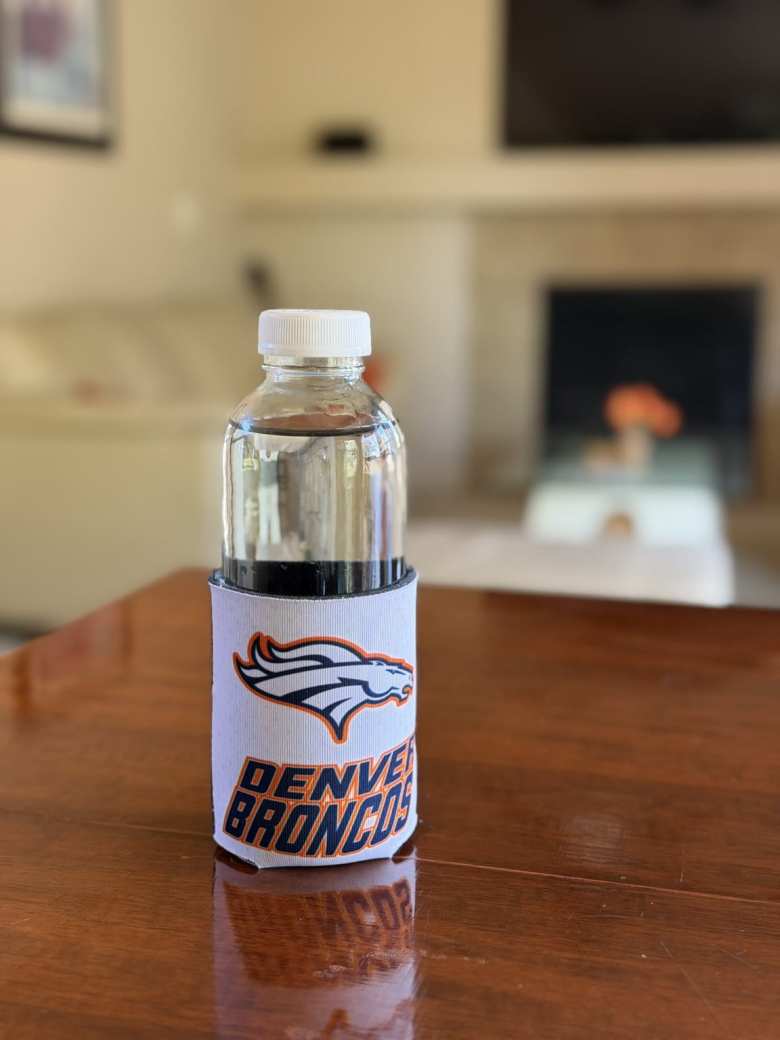 The clear glass bottle with Denver Broncos koozie.