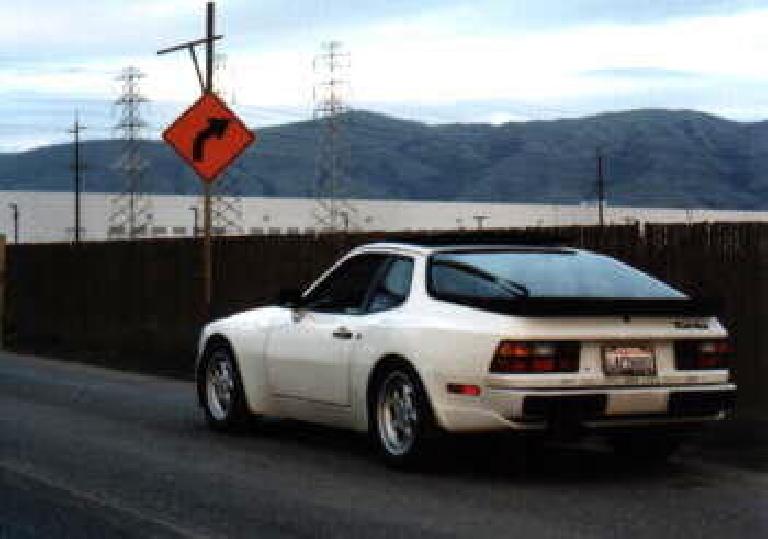 Right view view of white 1986 Porsche 944 Turbo in front of an orange turn right sign.