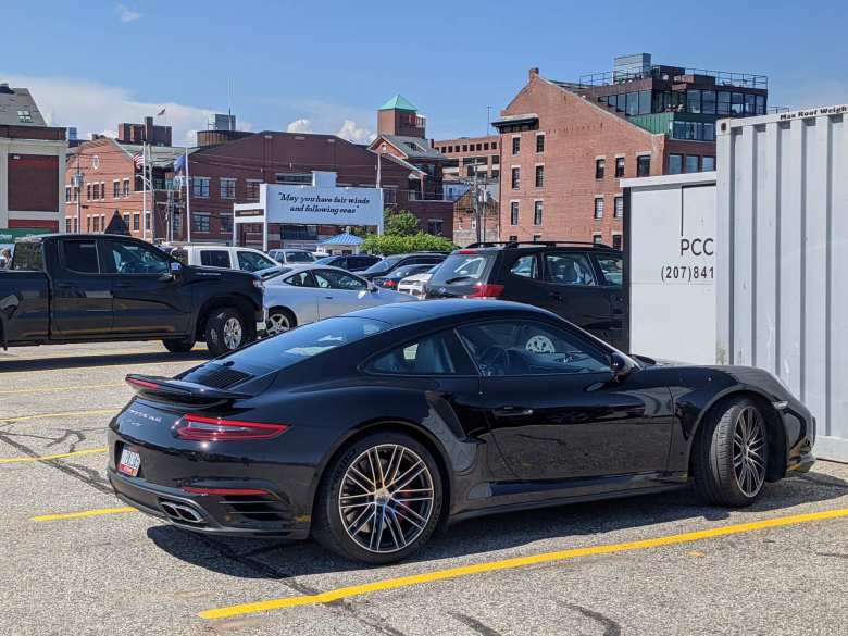 A black 911 Turbo (991 Series) parked in downtown Portland, Maine with a sign reading "May you have fair winds and following seas."