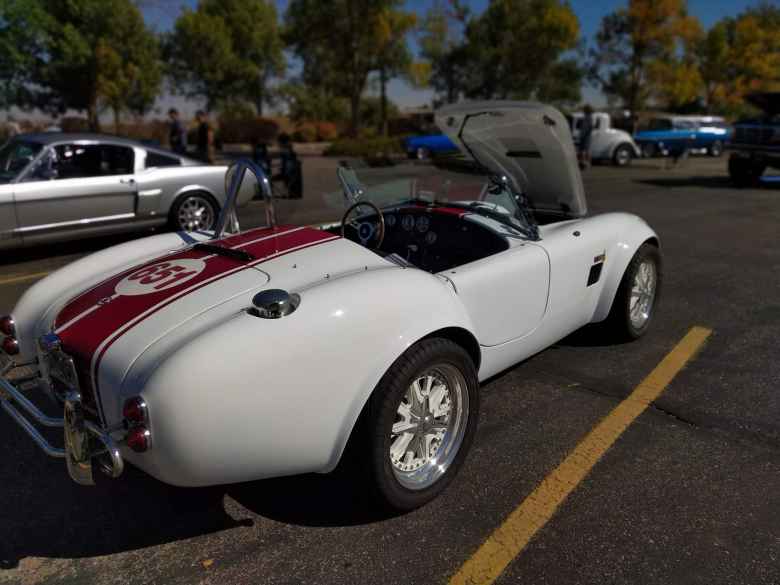 Rear view of the white AC Cobra replica with red racing stripes.