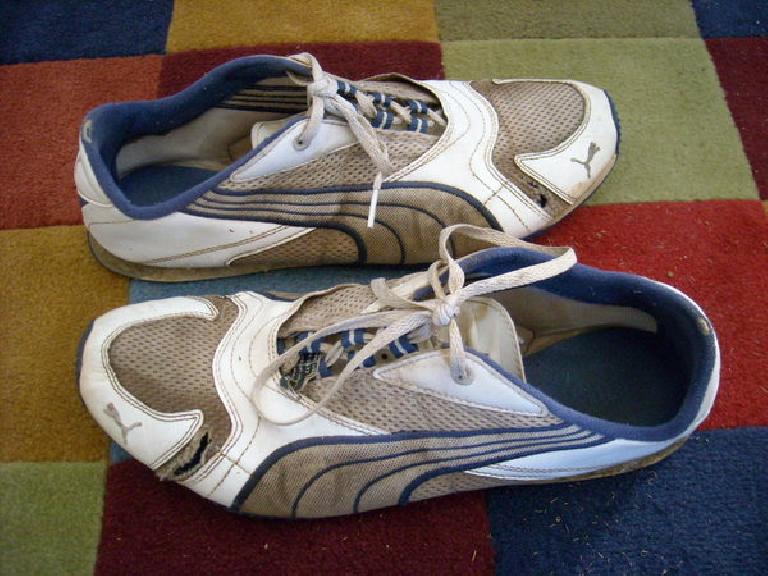 two dirty Puma Saloh shoes with rips in their fabric on colorful doormat