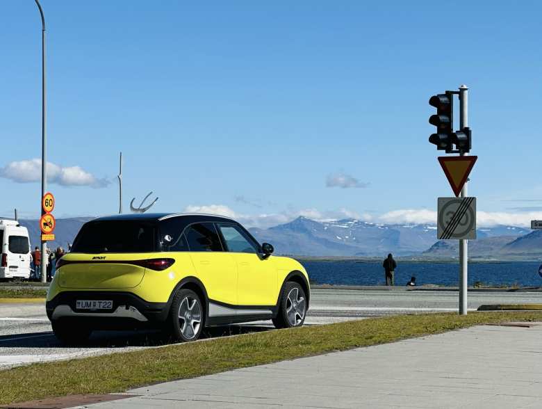 A yellow Smart #1 crossover SUV with the mountains on Videy island in the background.