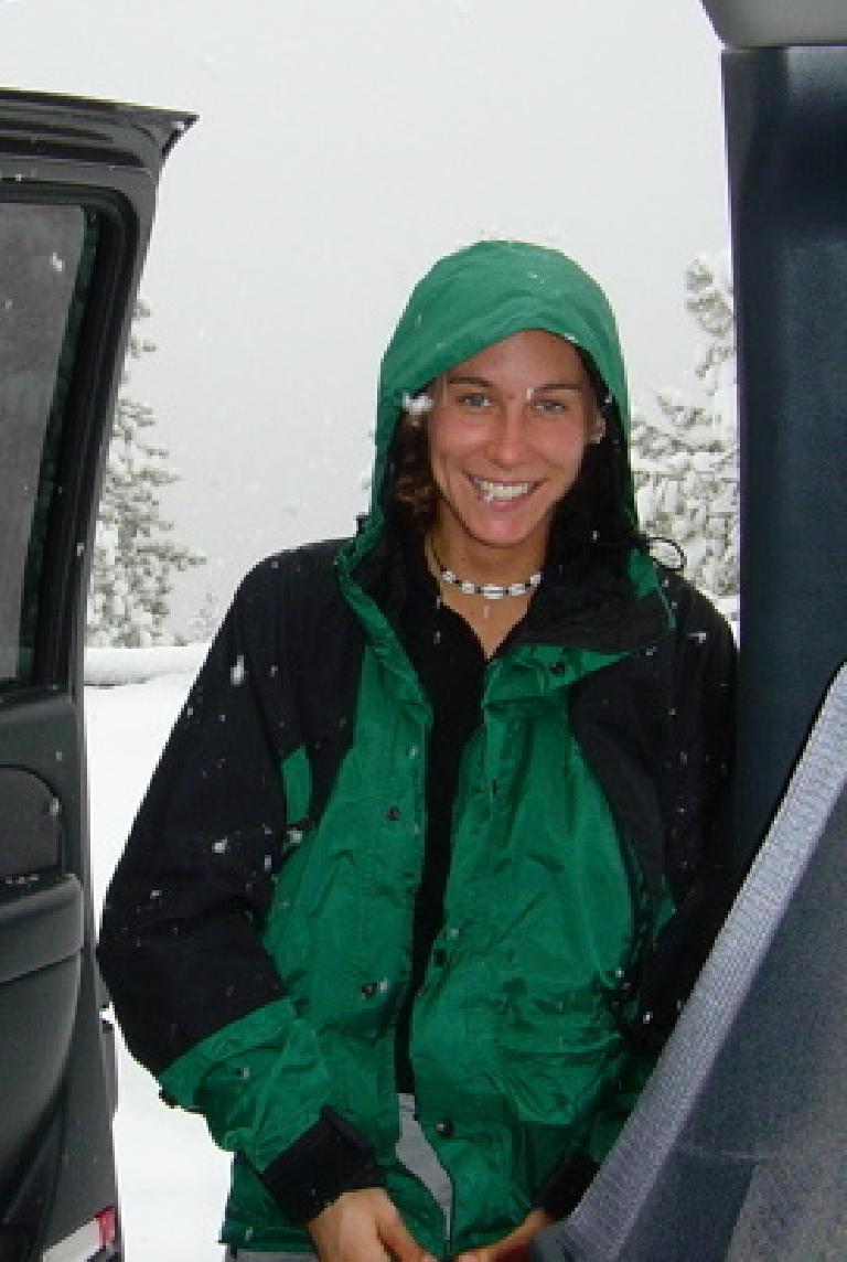 Rhea wearing a green parka standing outside a truck door with snow coming down