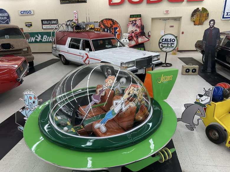 A model of the flying car used in the Jetsons. In the background is a 1984 Cadillac Fleetwood Hearse that was one of four vehicles used in the 2016 Ghostbusters movie. A model of the flying car used in the Jetsons. In the background is a 1984 Cadillac Fleetwood Hearse that was one of four vehicles used in the 2016 Ghostbusters movie.