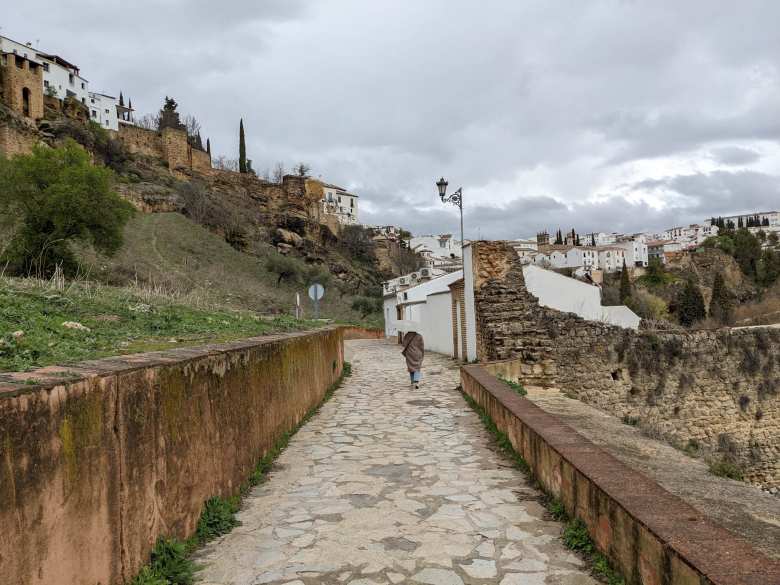 Andrea walking on a path towards the Baños Árabes and Puente Viejo with white houses of Ronda in the background.