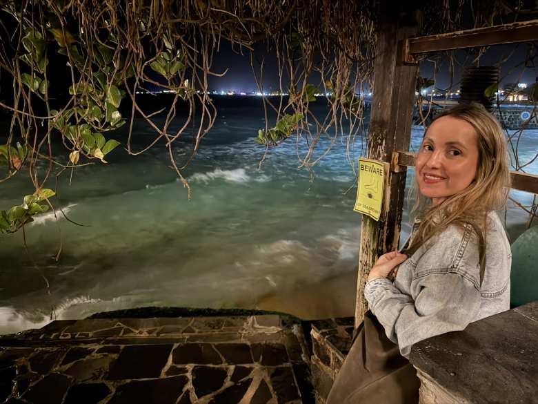 Andrea under a pergola by the ocean next to a sign that said 